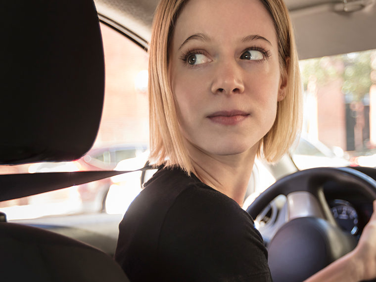 Female driver looking back to the rear of her car