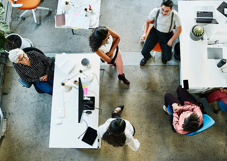 Overhead view of a group of workers gathering around desks to confer