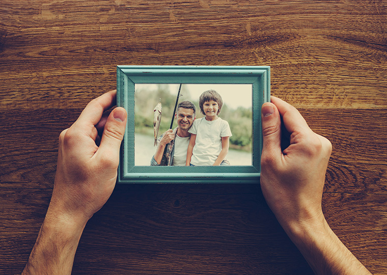 Hands holding a framed photograph of a father and son holding a fishing pole