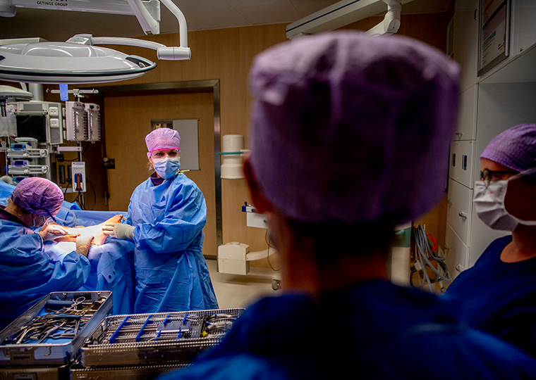 A female surgeon looks to two nurses as a male surgeon continues to work on a patient's foot.